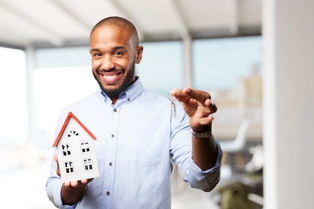 A smiling black man holding a key and a small block house.